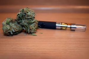 CBD oil for vape near me—cannabis buds beside vape pen cartridge with amber oil.