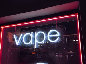 Treasure Coast Vape Shop neon sign glowing with bright white letters and red border in urban night setting