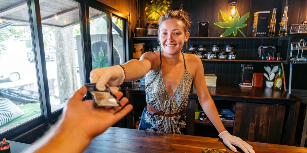 Smoke shop near me—customer receives package at counter with cannabis products displayed.